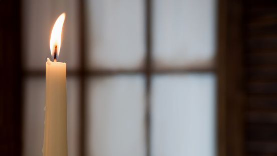 White high burning candle on a blurred background of a window with copy space