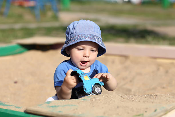 Child is playing with broken toy car in sandbox