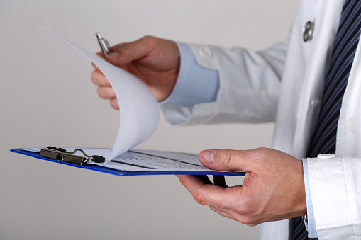 Male medicine doctor hand holding silver pen looking in clipboard closeup. Medical care, insurance, prescription, paper work or career concept. Physician ready to examine patient and help