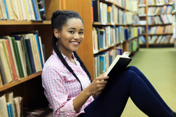 istock Smiling high school student reading on ground at the library 520747510