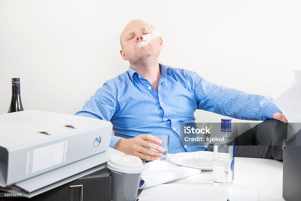 Businessman smokes and drinks at the office Office worker smokes cigarettes and drinks vodka. Achievement Stock Photo