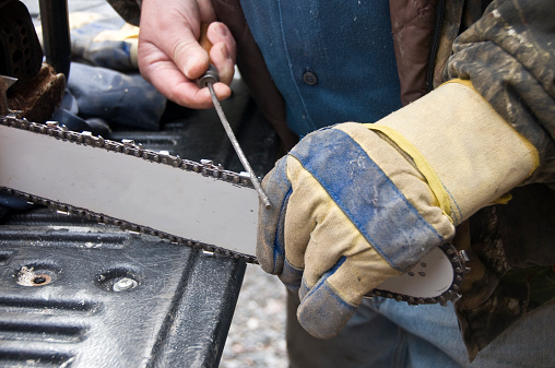 A man using a special file to sharpen the blades on a gas powered chainsaw chain