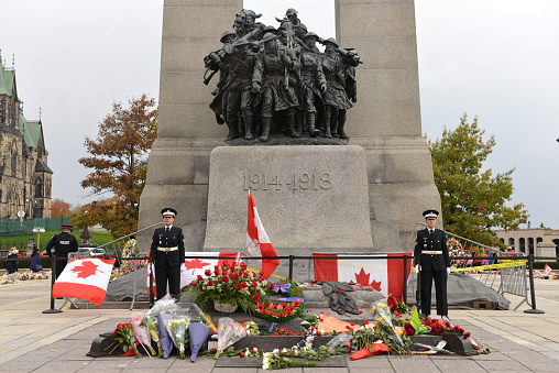 Ottawa, Canada - October 25, 2014:  Ceremonial guards stand at attention while mourners pay respect at the Ottawa Cenotaph where guard Nathan Cirillo was shot 3 days before.  An armed policeman, on the left, is also on site.