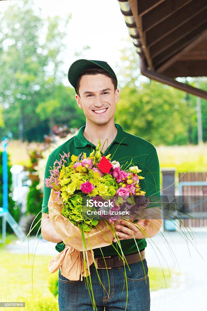 Delivery man delivering flowers Delivery man delivering a bouquet, standing in the entrance door and holding flowers, smiling at camera. Adult Stock Photo