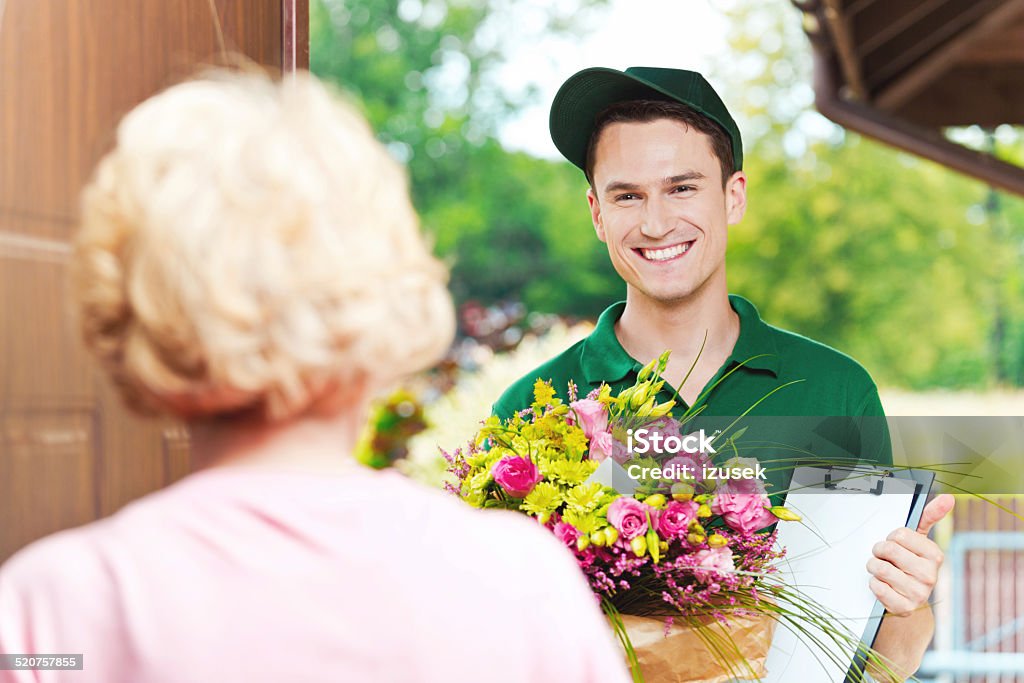 Delivery man delivering flowers Delivery man delivering a bouquet for mature woman, standing in the entrance door and holding flowers and clip board. Delivering Stock Photo