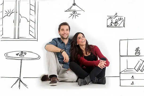 Young couple sitting on floor looking up while dreaming their new home and furnishing.