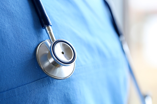 Stethoscope head lying on medicine therapeutist doctor chest wearing blue uniform closeup. Medical care, help or insurance, equipment shop or store concept. Physician waiting for patient to examine