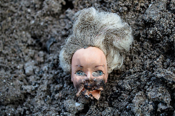 Melted plastic girl doll head lie in a pile of grey ash