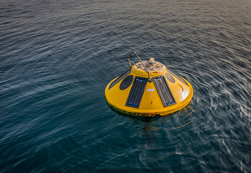 The image of small yellow buoy intended for weather and oceanographic observations. The buoy is ancored and is floating on sea surface. The image was shot in the Gulf of Trieste on a calm April day.