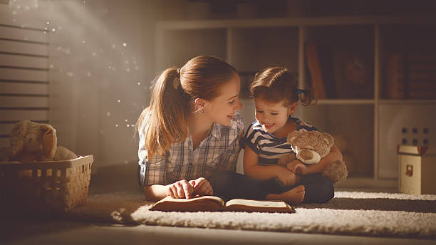 familia feliz madre con hija lea un libro en la noche - child bedtime imagination dark fotografías e imágenes de stock