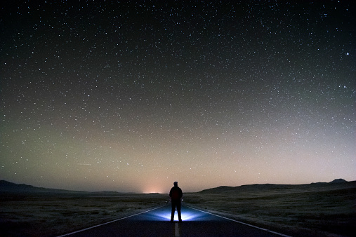 Lonely man standing in the middle of the road on the desert looking into the stars in search of the answer to ultimate question regarding his and mankind existence. High ISO at 3200.
