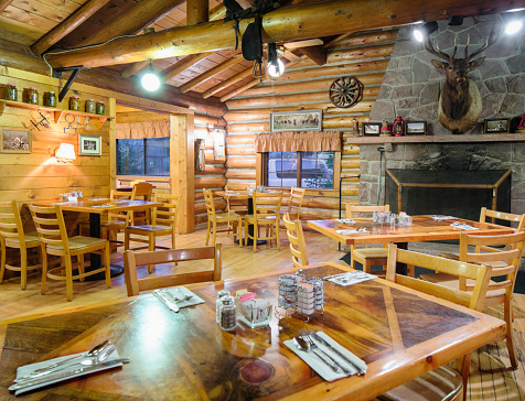 American Western log cabin restaurant dining room interior with a stone fireplace,deer head trophy, pickled vegetables and pictures on the wall.