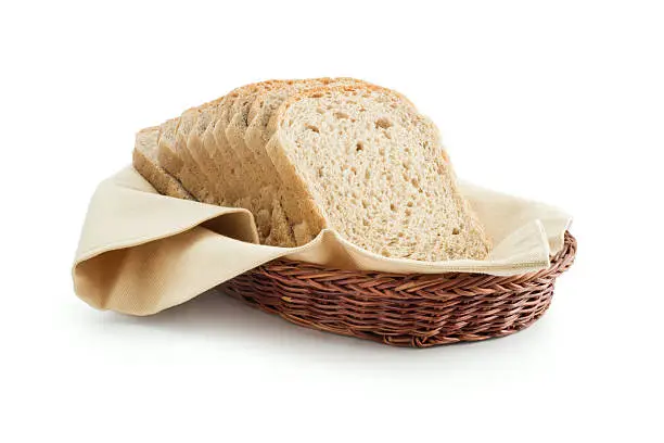 Wholemeal toast bread slices placed on a cotton cloth napkin in a wicker basket close up isolated on white background.