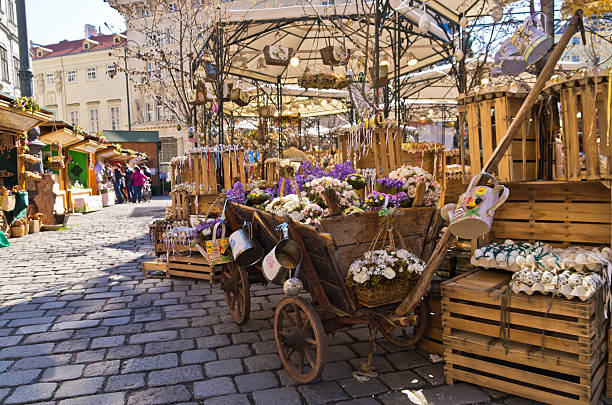 A moveable basket on wheels with delicate red flowers in it at the side of an old street