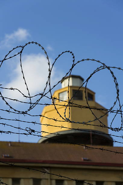 istock Guarding tower behind barbed wire fence around prison walls 520775376