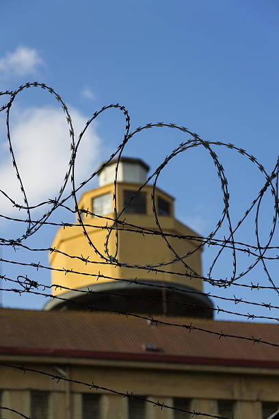 istock Guarding tower behind barbed wire fence around prison walls 520775882