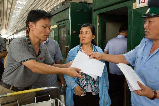 Dandong, China - Sep 06, 2014: A train conductor hands over forms to fill in to a North Korean citizen before the departure of the train to Pyongyang. Dandong station is located just a few kilometres from the Chinese-North Korean border. Only very few trusted DPRK citizens enjoy the privilege of travel to foreign countries.