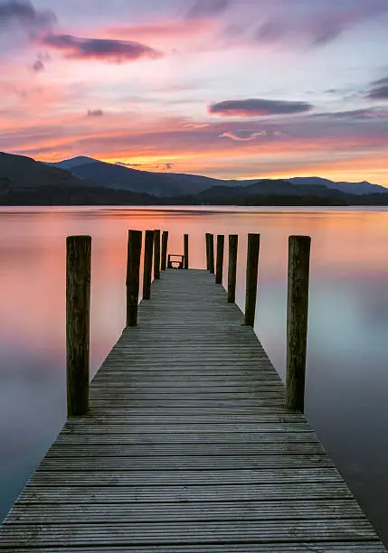 A beautiful vibrant pink and purple sunset with Ashness Jetty in the foreground at Derwentwater in the Lake District, UK.