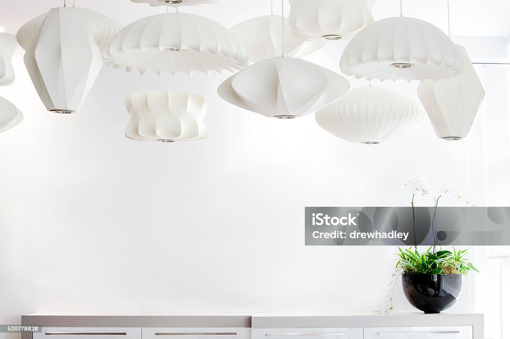 Group of suspended white lamp shades and orchid. Bright horizontal image of stylish lamp shades suspended  above a counter with a white orchid camera right. Space for copy. Electric Lamp Stock Photo