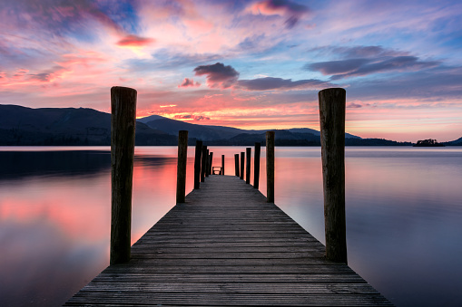 Ashness Jetty at Derwentwater, Keswick, Lake District, UK. The image features a wide angle view of the jetty with a stunning pink and purple dramatic sunset.