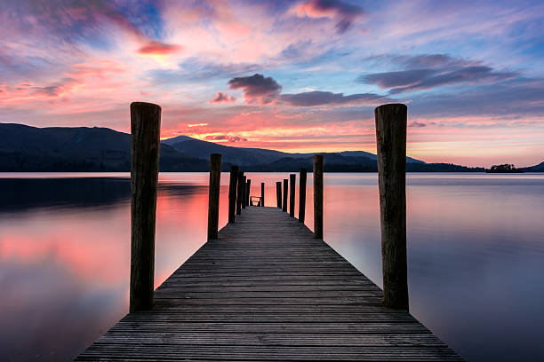 Ashness Jetty With Pink And Purple Vibrant Sunset. Ashness Jetty at Derwentwater, Keswick, Lake District, UK. The image features a wide angle view of the jetty with a stunning pink and purple dramatic sunset. derwent water stock pictures, royalty-free photos & images