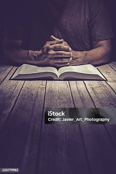 Man Praying On A Wooden Table With An Open Bible Stock Photo - Download Image Now - Praying, Bible, Book
