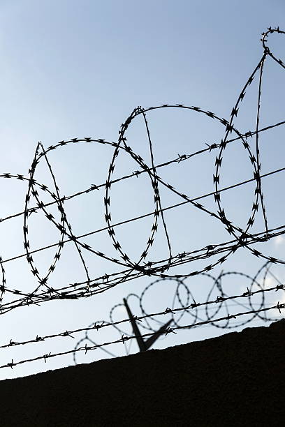 istock Prison wall barbed wire fence detail with blue sky background 520780022