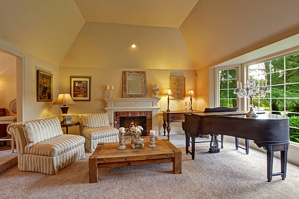 Luxury family room with grand piano and fireplace Luxury family room with high vaulted ceiling and large french window. Room has grand piano, fireplace, striped chairs and wooden coffee table expensive grand piano stock pictures, royalty-free photos & images