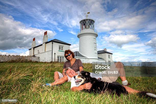 Mature Smiling Couple And Dog Sitting On Grassy Headland Stock Photo - Download Image Now