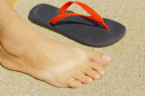 A man’s foot on the sand with the tan mark made by the sandal.   