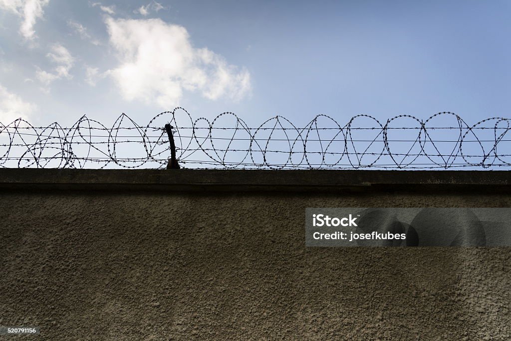 Prison wall barbed wire fence with blue sky background Prison wall barbed wire fence with blue sky in background Prison Stock Photo