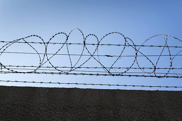 istock Prison wall barbed wire fence with blue sky background 520792670