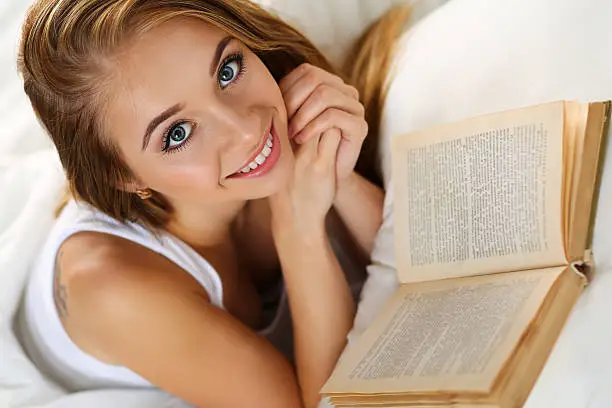 Photo of Young beautiful smiling blonde woman lying in bed reading book