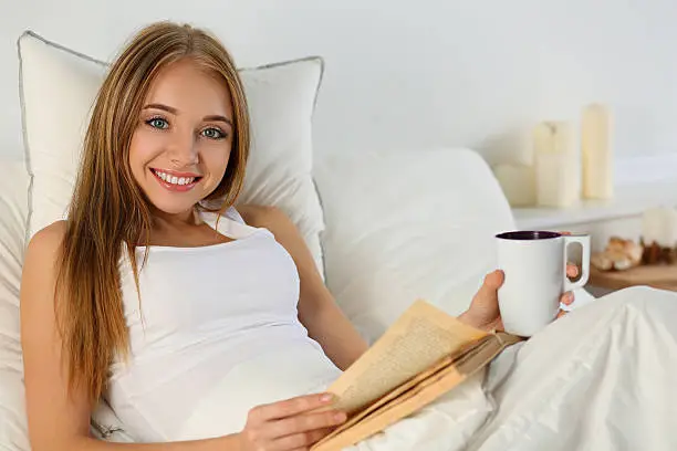 Photo of Young beautiful smiling blonde woman lying in bed reading