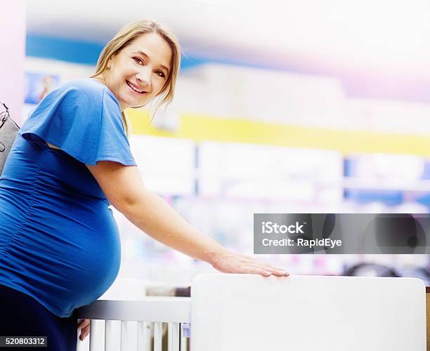 Pregnant Woman Smiles Choosing Cot In Baby Shop Stock Photo - Download Image Now - Crib, Store, 30-39 Years