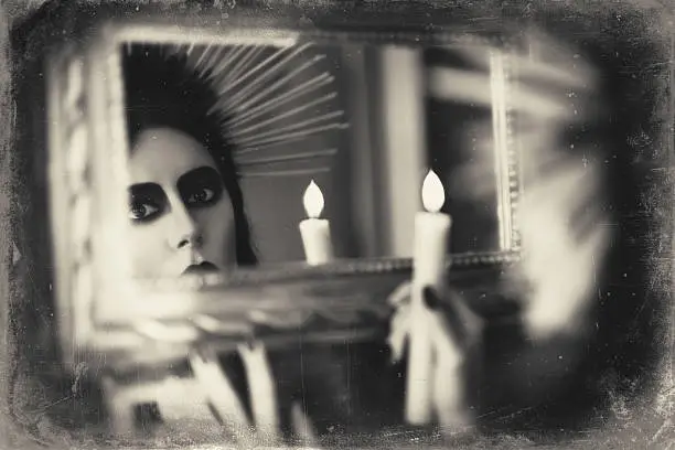 Beautiful goth girl holding candle in hand and looking into the mirror. Grunge texture effect