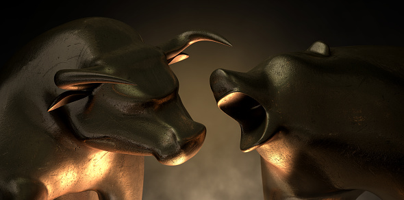 An abstract closeup of two gold cast statuettes depicting a stylized bull and a bear in dramatic contrasting light representing a financial market trends on an isolated dark background
