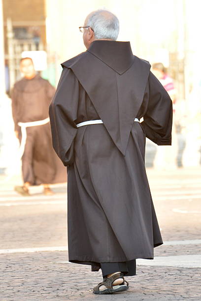 Monk in a brown habit with a hood Assisi, Italy - October 4, 2014: Monk with a gray hair, dressed with a brown habit with a hood, glasses and sandals on his feet walks through the pavament. gladiator shoe stock pictures, royalty-free photos & images