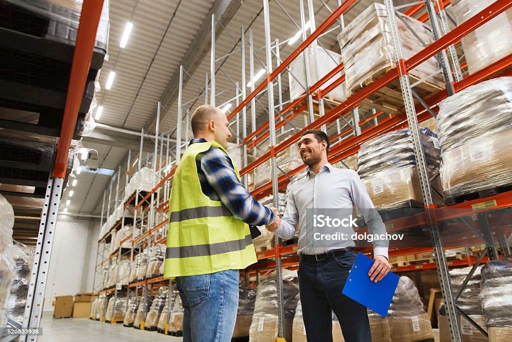 worker and businessmen with clipboard at warehouse wholesale, logistic, people and export concept - manual worker and businessmen with clipboard shaking hands and making deal at warehouse Handshake Stock Photo