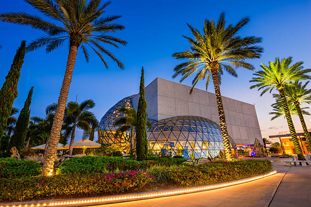 September 20, 2020 - St. Petersburg, Florida, United States of America USA: A general landscape view of Salvador Dali Museum in front of the St. Petersburg bay in a cloudy sunday raining day, with a row of palm trees  in front of the port view.\n\nSalvador Dali Museum in St. Petersburg, is the house of  the largest collection of work by surrealist painter outside Europe.\n\nThe unique modern architecture of the surrealist artist Salvador Dali is signed on the facade's design. The Museum is located in the downtown district along the waterfront.\n\nSt. Petersburg is 30 minutes to Sarasota downtown, one hour to Siesta Beach, one of the most famous beaches around United States. Also, just one hours driving from Tampa and four hours driving from Miami.\n\nNobody are at the streets because this photo was taken during the Corona Virus Pandemic illness.