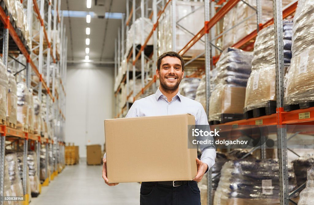 happy man with cardboard parcel box at warehouse wholesale, logistic, business, export and people concept - happy man with cardboard parcel box at warehouse Storage Room Stock Photo