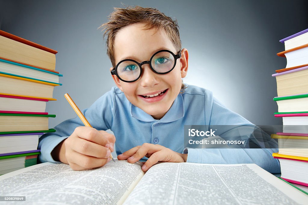 Clever schoolkid Portrait of cute lad in eyeglasses making notes in book during reading Book Stock Photo