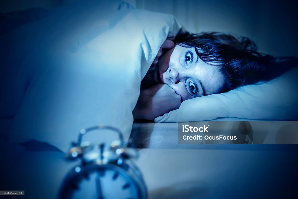 woman in bed eyes opened suffering insomnia and sleep disorder young woman in bed with alarm clock and eyes opened suffering insomnia and sleep disorder thinking about his problem on dark studio lighting in sleeping and nightmare issues Horror Stock Photo