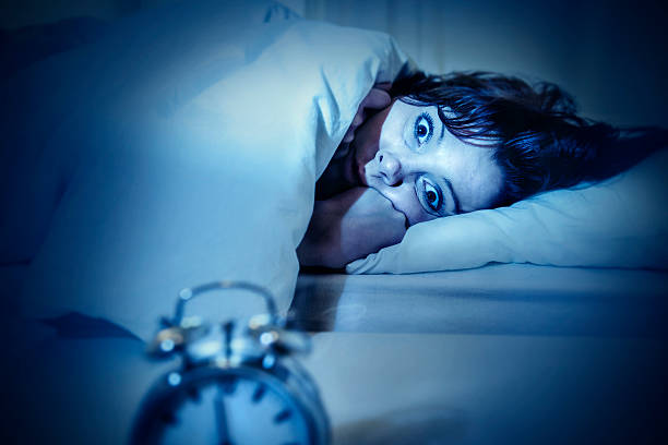 woman in bed eyes opened suffering insomnia and sleep disorder young woman in bed with alarm clock and eyes opened suffering insomnia and sleep disorder thinking about his problem on dark studio lighting in sleeping and nightmare issues horror waking up bed women stock pictures, royalty-free photos & images