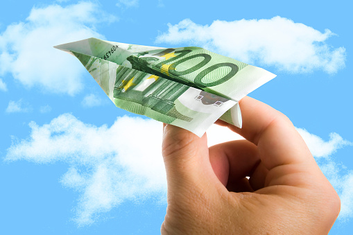 Man Hand Holding Banknote Paper Plane making it fly on a blue sky with clouds in wealth , money income, benefits and financial concept or low cost travelling add