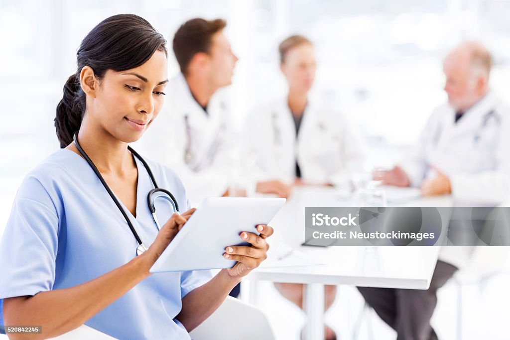 Nurse Using Digital Tablet With Medical Team Discussing In Boardroom Young nurse using digital tablet with medical team discussing in background in hospital. Horizontal shot. 20-24 Years Stock Photo