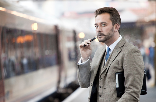 Young trendy businessman travelling to work smoking an e-cigarette.
