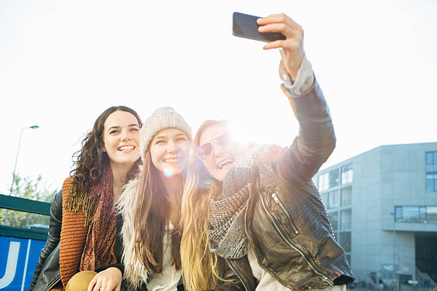 three cute teenage girls sitting on a railing from the U-Bahn in Berlin and photographing themselves with a smart phone