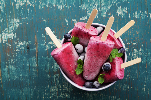 Homemade blueberry ice cream or popsicles decorated green mint leaves on teal rustic table, frozen fruit juice, vintage style, top view