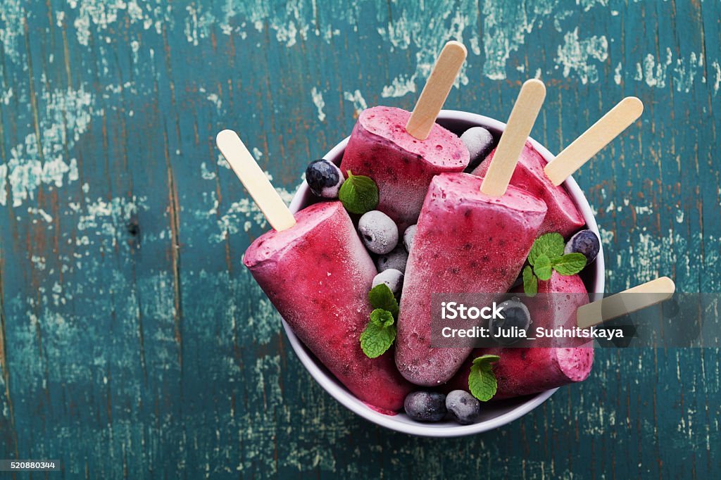 Ice cream from blueberry, frozen fruit juice, vintage style Homemade blueberry ice cream or popsicles decorated green mint leaves on teal rustic table, frozen fruit juice, vintage style, top view Flavored Ice Stock Photo